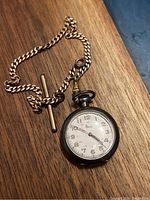 Top view of vintage Elco silver pocket watch face with attached chain and T-bar, showing watch dial and hands.