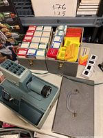 Argus 300 projector with attached power cord, numerous vintage family photo slide boxes in metal case, and loose slides on a table