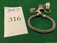 Lot overview with sterling silver woven bracelet and four sterling rings placed on green background with lot number card.