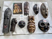 All nine African wood masks arranged on white background with the reference book to the top-left.