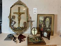 Wide view of lot showing large gilt framed crucifix with bubble glass, rosaries, framed religious prints, and triptych on white background