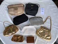 Overview of all eight vintage purses and one leather wallet on a white tablecloth, showing variety of materials and colors including gold metallics, black beads, white beads, and brown leather wallet.