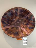 Front view of the round metal wall plate showing the flame-inspired abstract painting in shades of copper, purple, and gold with circular and interwoven curved motifs.