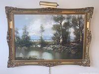 Full view of landscape oil painting in ornate gold gilt frame with attached brass picture light