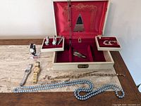 Overview of the lot showing vintage jewelry box with red velvet interior, watches, necklaces, and costume jewelry laid out on wooden surface.