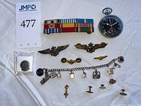 Overview of lot: ribbon bar, pocket watch, pins, wings, bracelet, buttons on white cloth