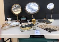 Wide view of all items showing mirrors, soap dishes, toothbrush holder, fan, and perfume bottle arranged on table.