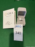 Moissanite report and ring box with ring inside, showing lot number card.