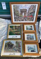 Photo of seven framed art prints including one large natural wood frame with Paris street scene and Arc de Triomphe, two gold-tone framed Monet prints, and four smaller natural wood framed Paris views.