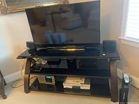 Full front view of Sony 40" LED TV on a black TV stand with included remote and AV components visible on shelves.