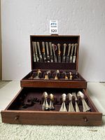 Wooden chest with hinged lid open showing knives in top tray and various forks and spoons in lower drawer