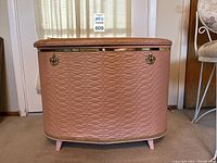 Front view of vintage pink Counsel hamper with quilted pattern, metal clasps, short angled legs.