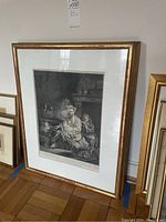 Framed antique black and white art print leaning against a wall, visible gold-colored frame and matting around the print.