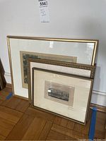 Three framed artworks leaning against the wall showing different sized prints with various matting and gold frames.