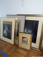 Four framed vintage ballet-themed artworks leaning against a wall on parquet floor, including black-and-white and color photos in various frame sizes