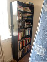 Front view of tall black bookcase with multiple shelves fully filled with various books.