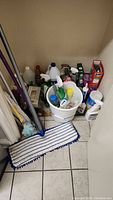 Whole lot showing mop, bucket, and assorted cleaning products on floor corner.
