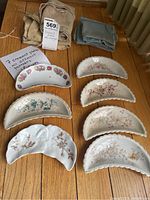 Full set of 7 crescent plates arranged on wooden floor with 5 fabric packing sleeves nearby