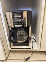 Front view of the Mr. Coffee electric drip coffee maker showing the digital control panel with buttons and the glass carafe in place.