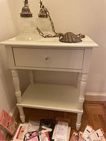 Front view of white wooden end table with drawer and lower shelf, light fixture on top