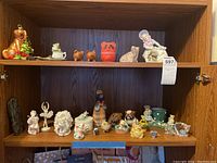 Shelf view showing a variety of assorted figurines including animals, children, ballerinas, and novelty items arranged on two shelves.