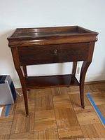 Front view of vintage wooden telephone table with drawer and curved legs on a parquet floor.