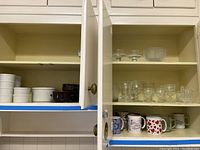 Cupboard with white ceramic soup crocks, glass bowls on middle and upper shelves, and assorted mugs on lower shelf.