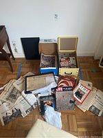 Wide view of collection spread on floor showing newspapers, magazines, framed historic document, and boxes for storage.