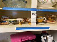 Italian decorative cups and plates arranged on a kitchen shelf, showing multiple cups with pedestal-style bases and colorful matching plates.