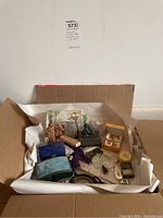 Photo showing a collection of small boxes, carved cameo shells, metal medallions, small figurines, and a decorative tile inside a cardboard box with tissue paper