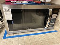 Front angle view of Oster microwave showing stainless steel and black glass door with control panel on the right side, placed on kitchen counter.