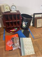 Photo showing desktop clocks, wooden mail sorter, floral trash can, assorted binders and photo albums on floor