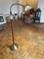 Full view of the floor lamp showing brass base, wooden pole, and adjustable brass lamp head in a room with wooden parquet flooring.