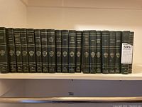 23 volumes of The Harvard Classics deluxe edition arranged on white shelves. Close views of spines show titles, edition, and emblem.