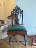 Front view of vintage wooden Gothic chair with carved pointed backrest and green upholstered seat. Minor wear visible on wood and upholstery.