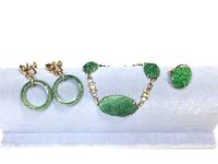 Pair of jade hoop earrings, jade bracelet and jade ring displayed on white stand