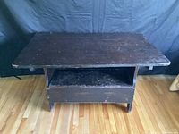 Closed view of dark wooden tilt top table bench with flat rectangular top surface and lower front shelf.