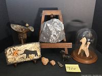 Full grouping of items on black background showing all ten pieces including fern fossil on easel, painted slate, metal vessel, miniature horse, terracotta quadriga with dome, carved stone faces, and arrowhead.