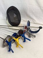 Photo showing all 6 items: 4 foil swords with colored grips (blue and yellow), 1 practice sabre, and fencing mask