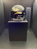 Full front view of glass sphere on black rotating pedestal with ruler for scale