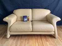 Front view of butter yellow Italian leather loveseat with two objects on left seat cushion for scale (shoe polish and shoe box).