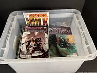 Plastic bin filled with Marvel comics including Deadpool and Iron Man 2.0 Fear Itself issue visible on top.