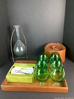 Full lot overview showing green brandy snifters, teak tray, ice bucket, floating glass bottle on metal stand, and boxed plates.