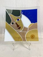 Front view of square decorative plate with abstract female figure in glass colors including blue, mustard yellow, and green.