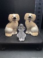 Front view of two Staffordshire confetti coat dogs and one frosted crystal poodle figurine, all displayed on a dark surface with measurement scale in the background.