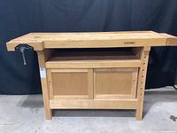 Front view of the WhiteGate carpentry bench, showing the front cabinet with sliding doors and one wood vice on the left side.