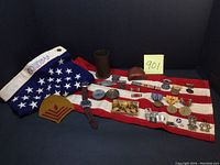 Overall collection showing folded US flag, medals on white bars, leather compass case, sergeant rank patches and wristwatches arranged on flag.