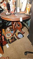 Full view of antique wooden round accent table showing table top and carved tripod base.