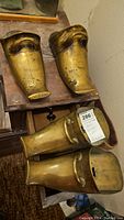 Photo showing pair of brass stirrups shaped like Conquistador foot armor placed on a wooden surface.