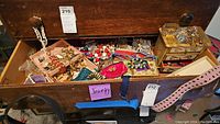 Wide view of wooden drawer containing assorted costume jewelry including necklaces, bracelets, earrings, bangles, and small jewelry boxes and trays.